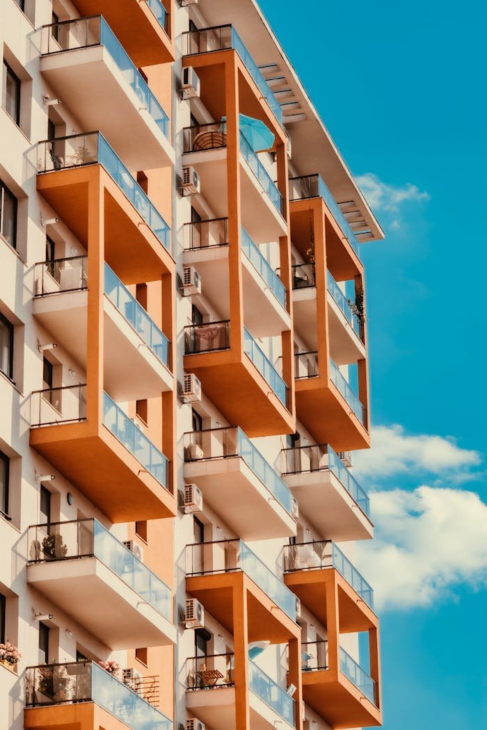 Low angle facade of modern brown and white condominium building with glass balconies against cloudless blue sky